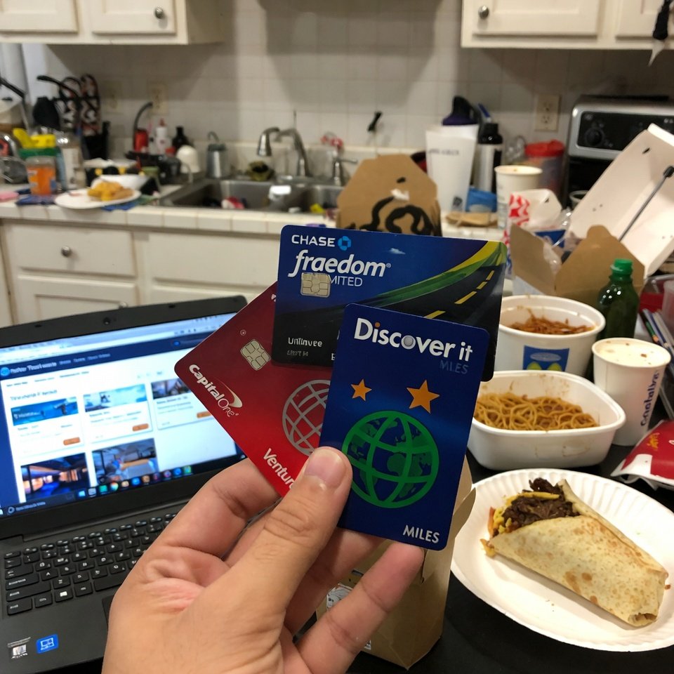 Person holding three travel credit cards in messy kitchen